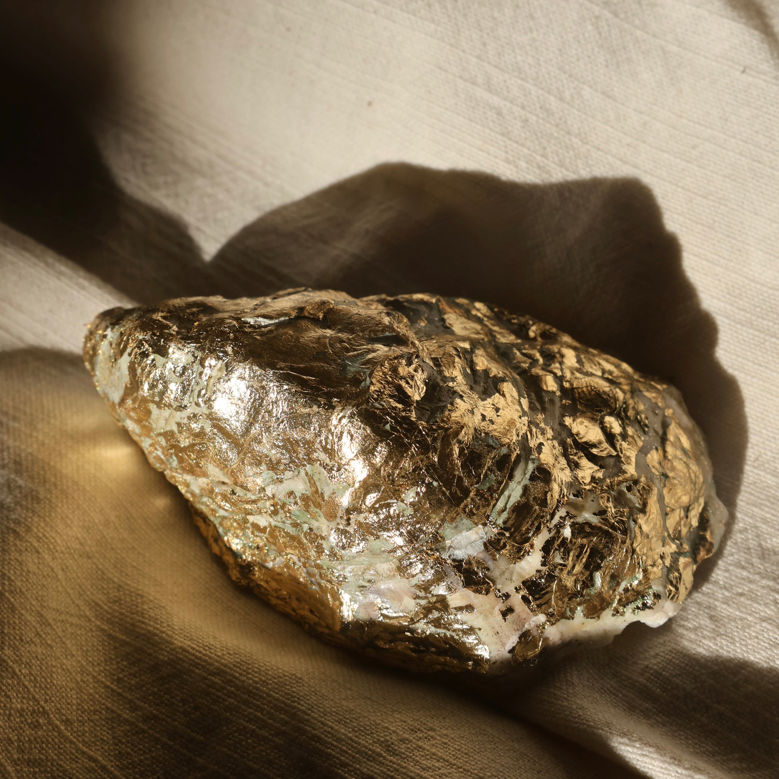 Golden foil-wrapped oyster shell candle by Lily Glow Home Decor reflecting natural light