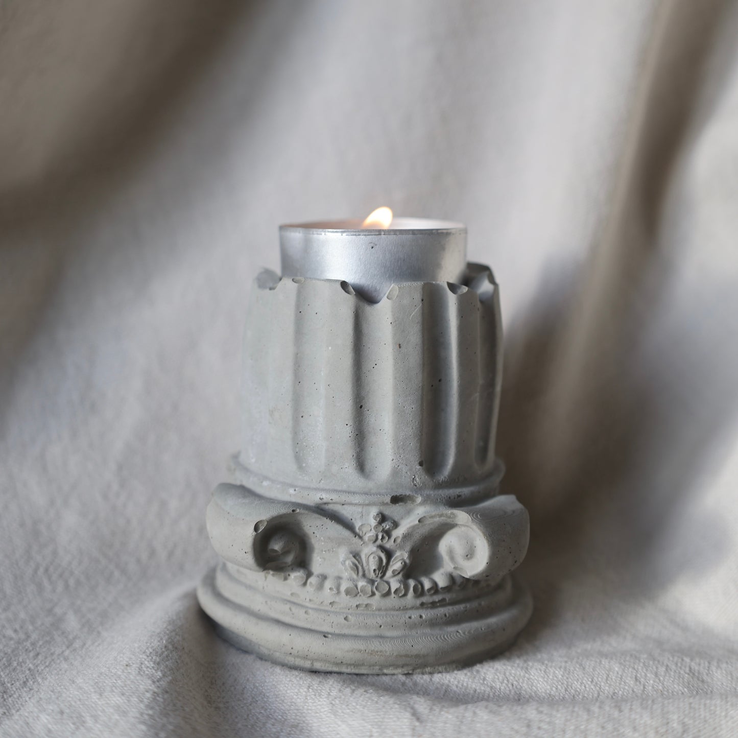 Decorative concrete column candle holder with a lit tealight on neutral fabric background by Lily Glow Decor