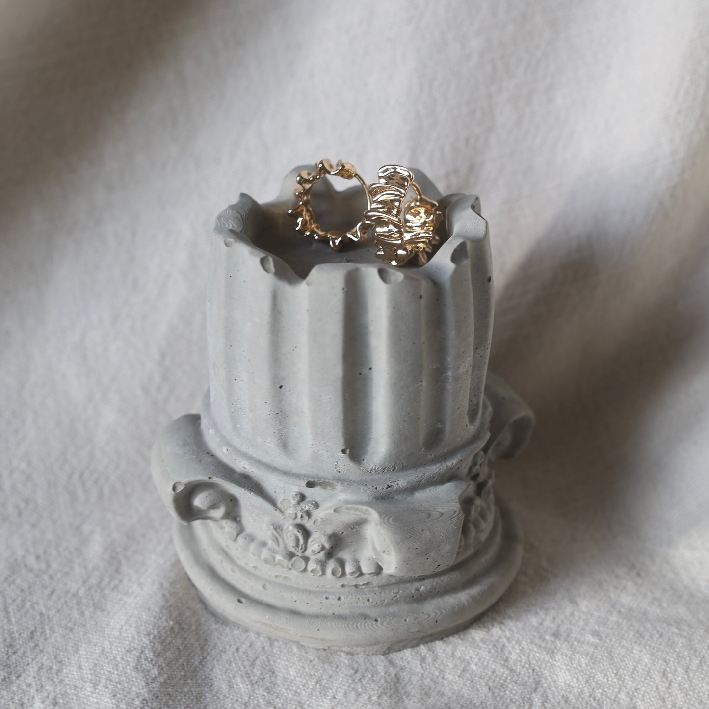 Decorative concrete column candle holder with a lit tealight on neutral fabric background by Lily Glow Decor