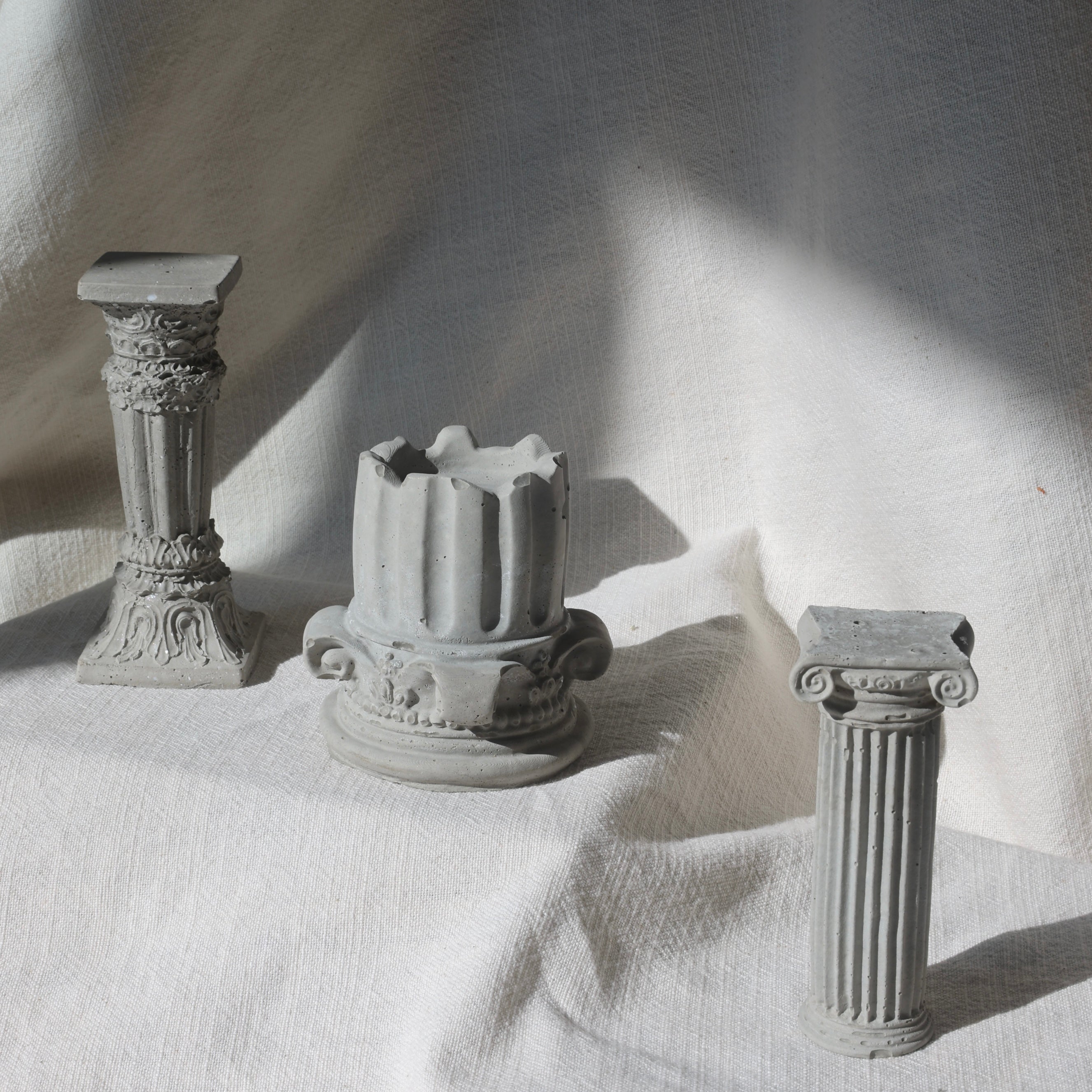 Set of three classical-style decorative columns made of concrete on light textured fabric by Lily Glow Home Decor
