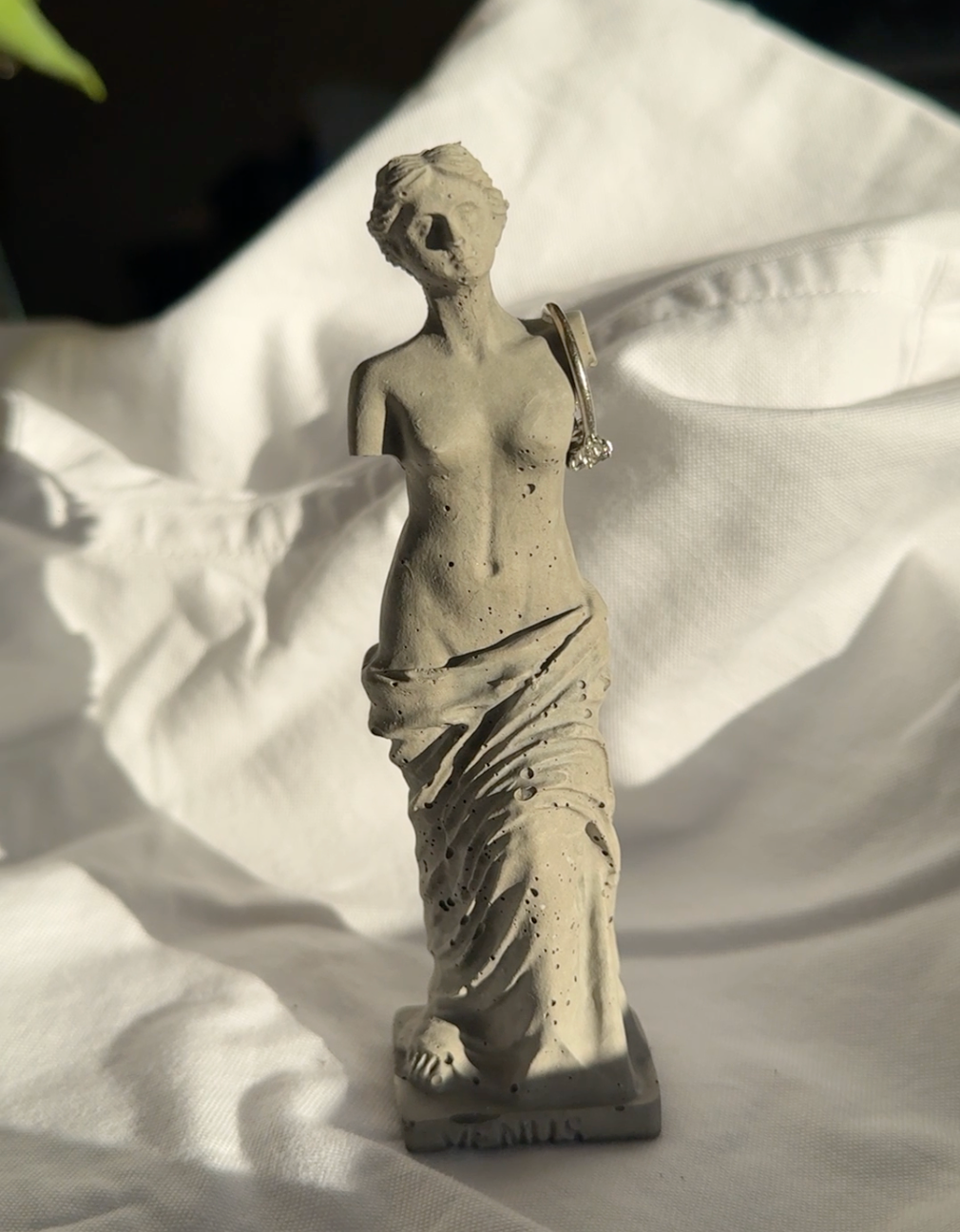 Concrete Venus statue with minimal texture on white fabric background, styled as a decorative element or ring holder.by Lily Glow Decor
