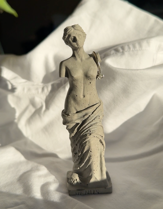 Concrete Venus statue with minimal texture on white fabric background, styled as a decorative element or ring holder.by Lily Glow Decor