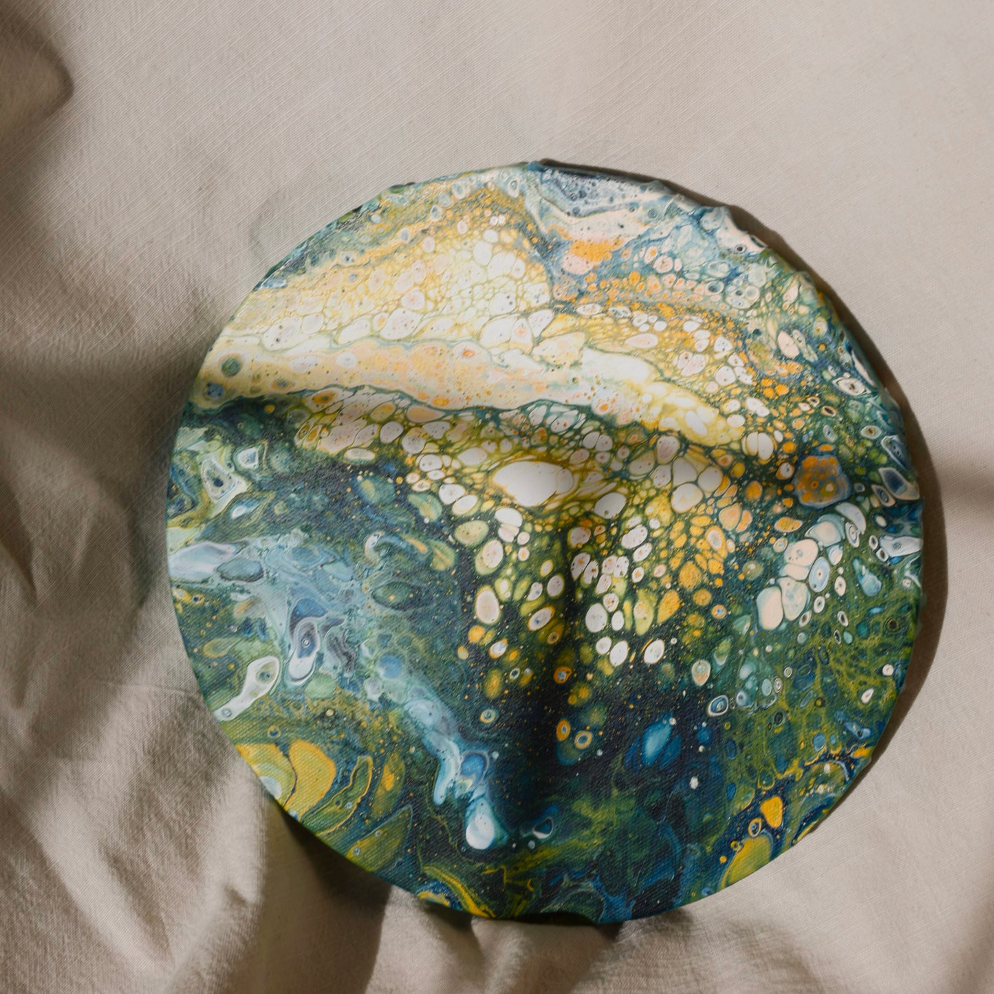 Close-up of a round canvas artwork with vibrant green and yellow abstract pattern on fabric background by Lily Glow Decor