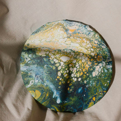 Close-up of a round canvas artwork with vibrant green and yellow abstract pattern on fabric background by Lily Glow Decor