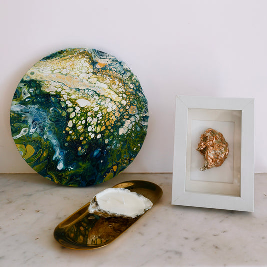 Round abstract painting in shades of green, yellow and white, placed on a marble surface next to home decor pieces by Lily Glow Decor