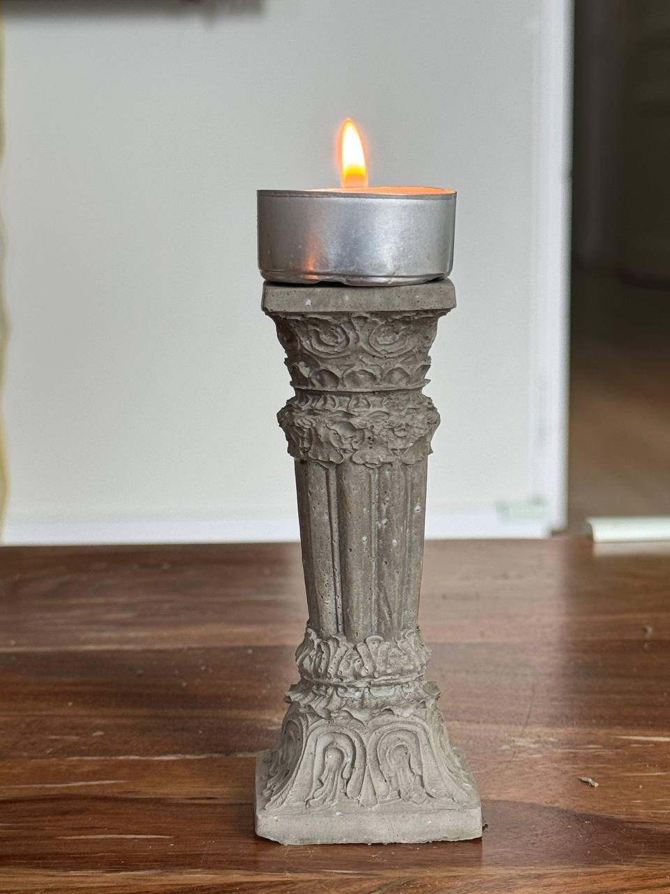 Concrete Corinthian-style candle holder with a lit tealight, placed on a wooden surface