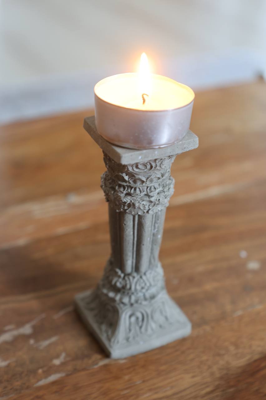 Concrete Corinthian-style candle holder with a lit tealight, placed on a wooden surface by Lily Glow Decor