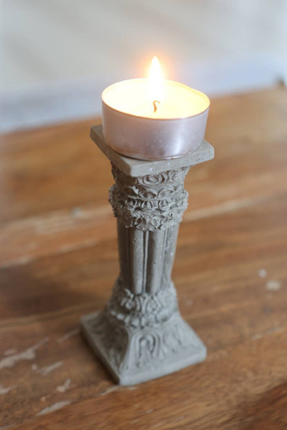Concrete Corinthian-style candle holder with a lit tealight, placed on a wooden surface by Lily Glow Decor