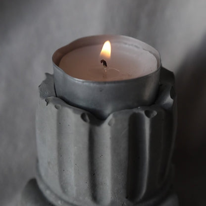 Decorative concrete column candle holder with a lit tealight on neutral fabric background by Lily Glow Decor
