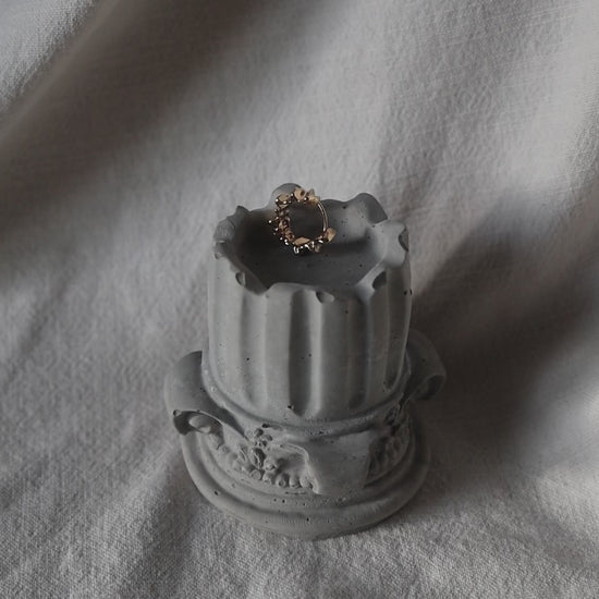 Decorative concrete column candle holder with a lit tealight on neutral fabric background by Lily Glow Decor