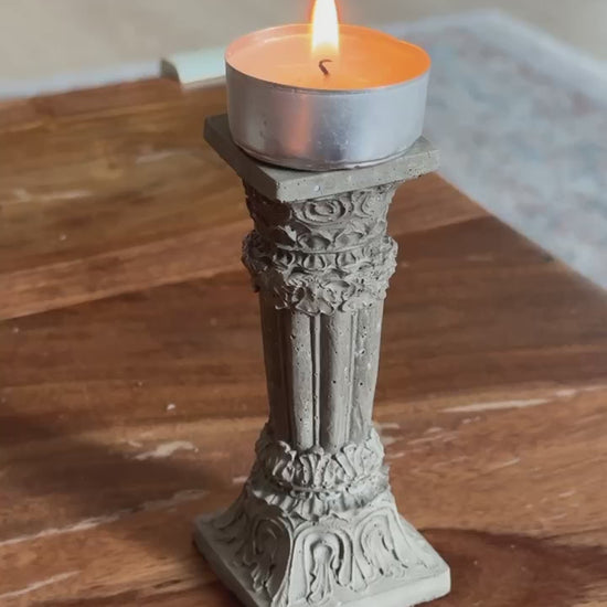 Concrete Corinthian-style candle holder with a lit tealight, placed on a wooden surface