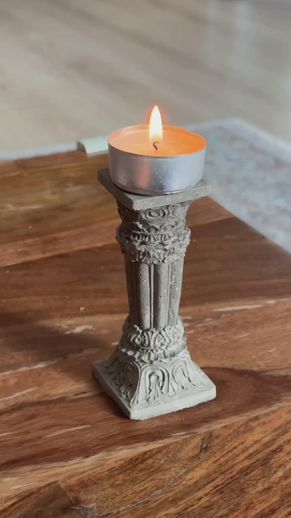 Concrete Corinthian-style candle holder with a lit tealight, placed on a wooden surface