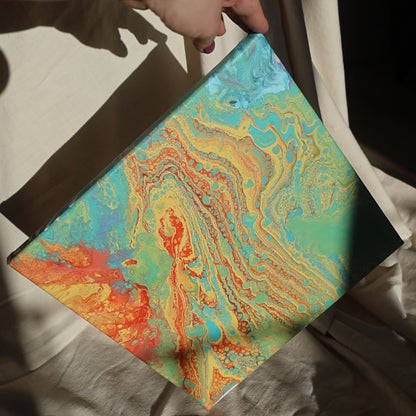 Abstract painting in 30x30 cm format with fluid patterns in blue, green, orange and beige tones, displayed against soft beige fabric by Lily Glow Decor