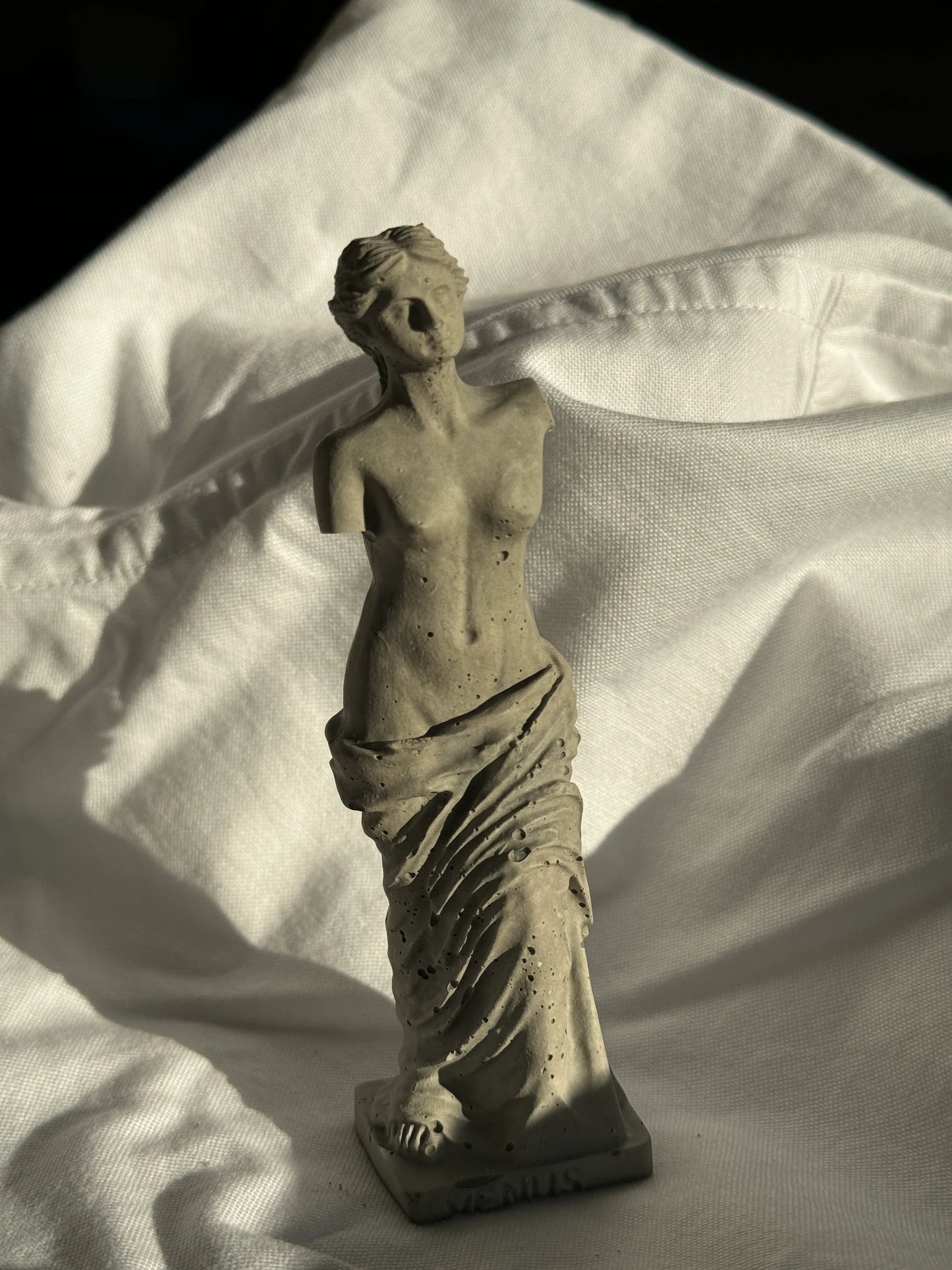Concrete Venus statue with minimal texture on white fabric background, styled as a decorative element or ring holder.by Lily Glow Decor