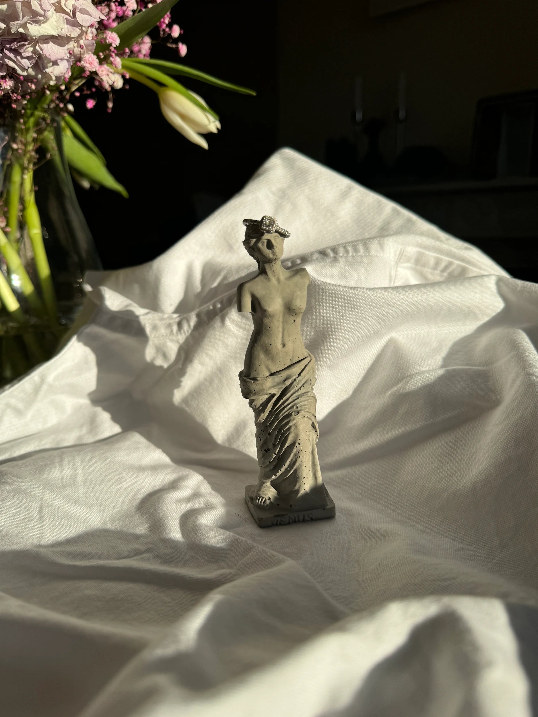 Concrete Venus statue with minimal texture on white fabric background, styled as a decorative element or ring holder.by Lily Glow Decor